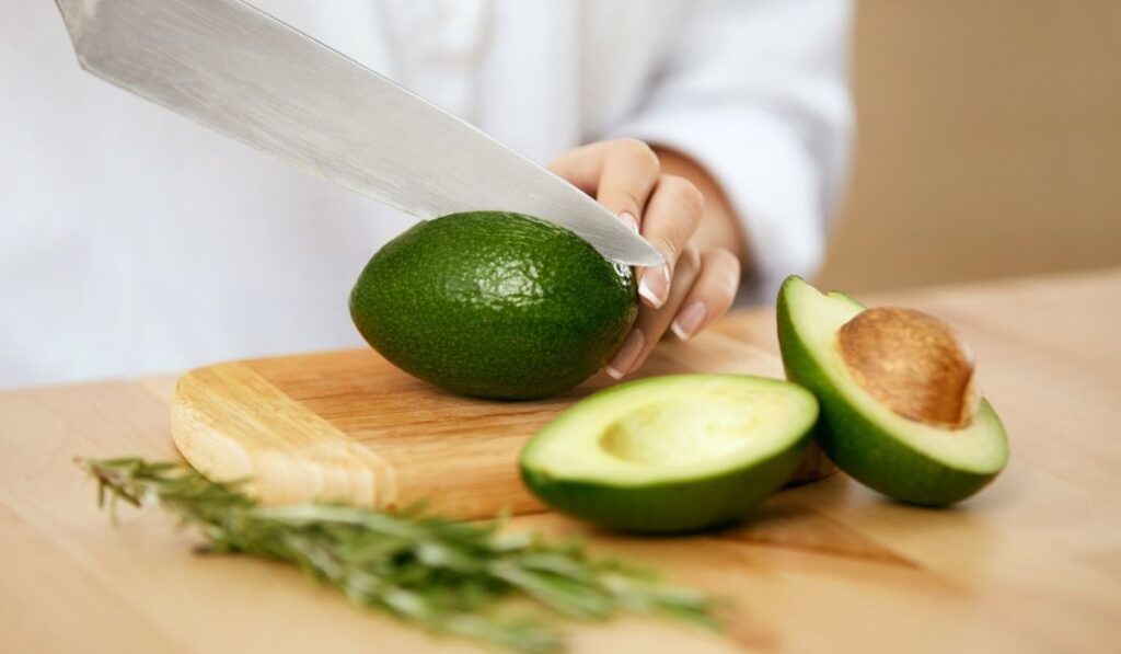 Female Hands Cutting Avocado In Kitchen