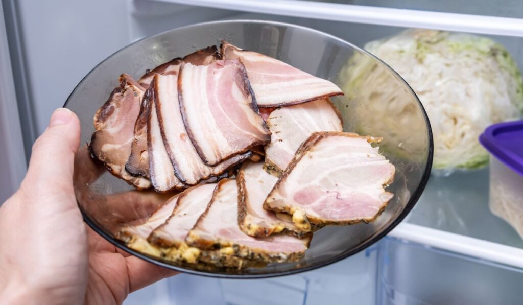 Hand putting sliced boiled cooked meat, bacon into the fridge for storage