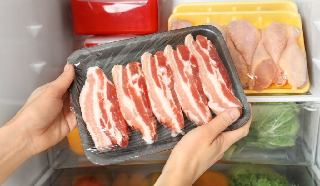 Woman taking raw bacon from refrigerator