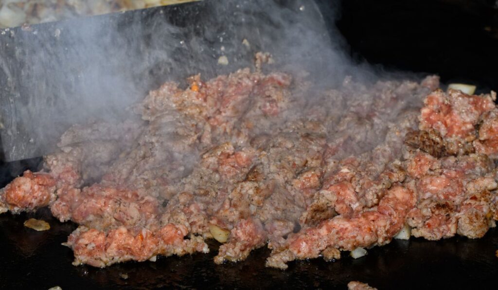 Ground sausage being cooked on griddle in preparation for breakfast casserole